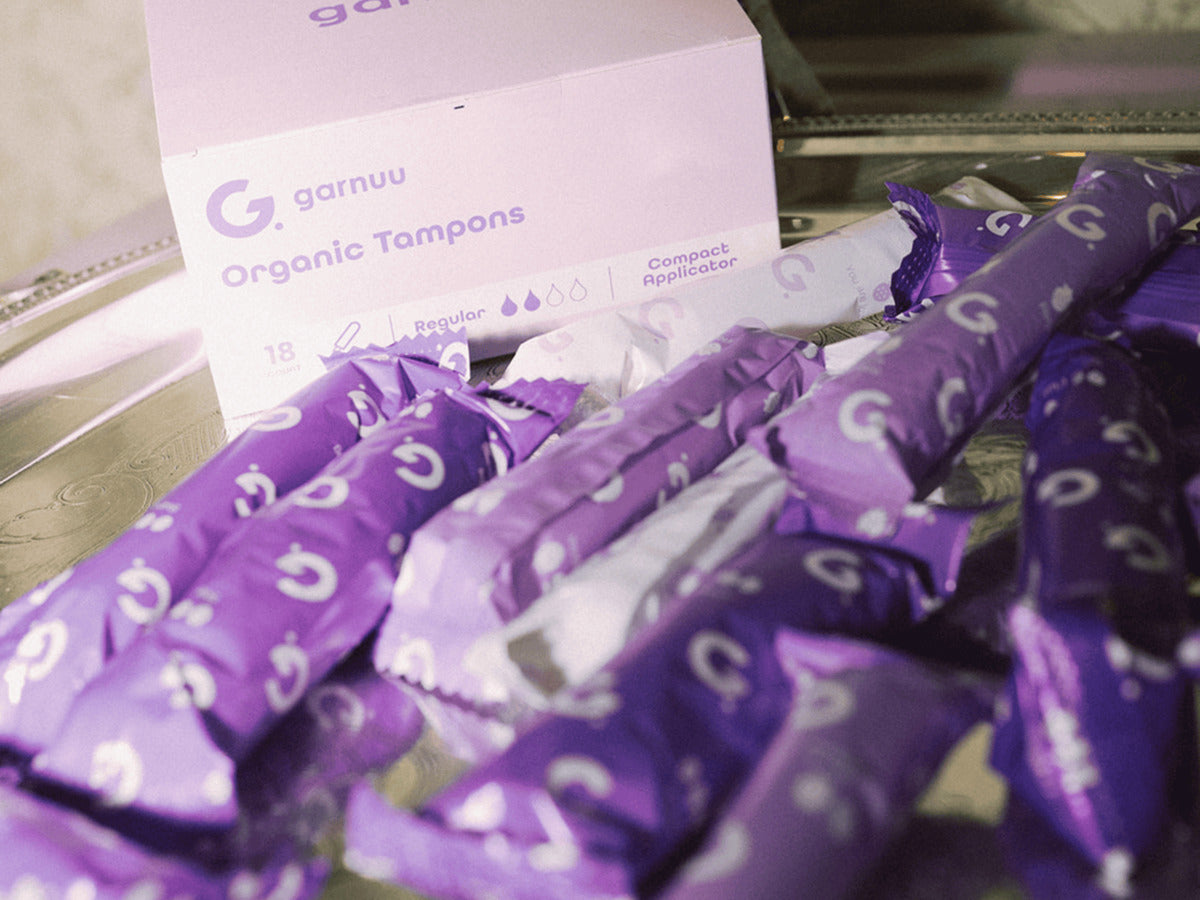 The Garnuu Organic Tampons box, marked 18 Regular, Compact Applicator, beside a pile of individually wrapped tampons
